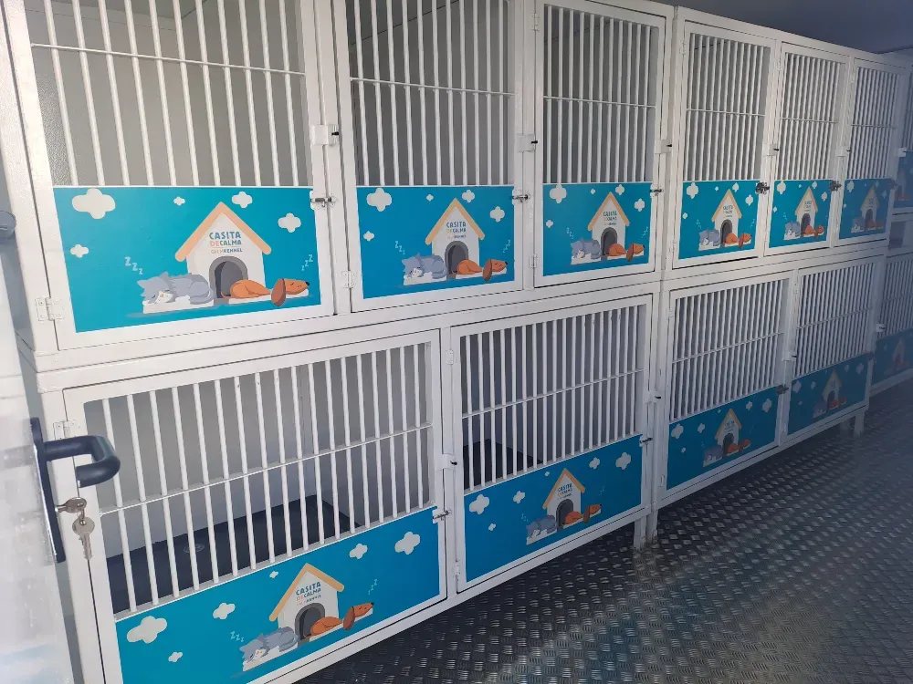 Casetas para mascotas de metal blanco con diseño de casa azul y blanca, dentro de un edificio.