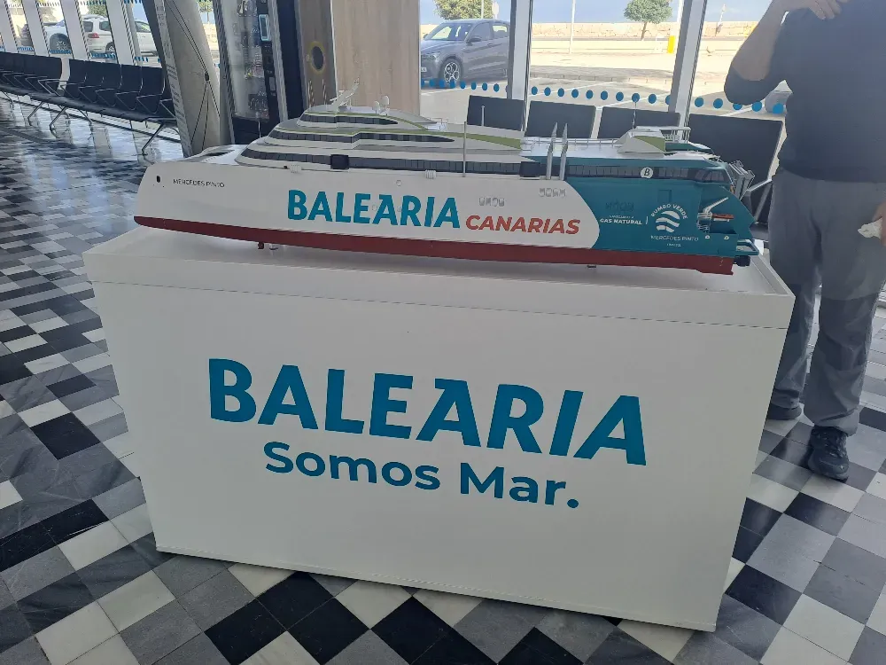 Maqueta de un ferry de Balearia Canarias sobre un soporte blanco. El soporte luce el logotipo de Balearia. 