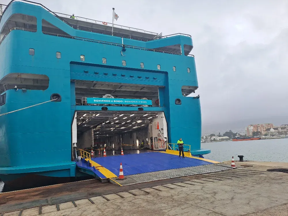Un ferry verde azulado atracado en un puerto, con la rampa bajada y en el que se veía a una persona .