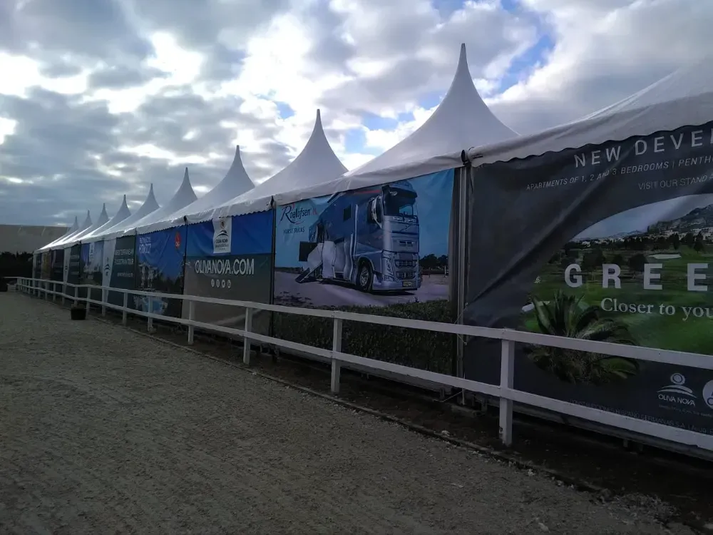Largas carpas blancas con pancartas publicitarias a lo largo de una valla blanca.