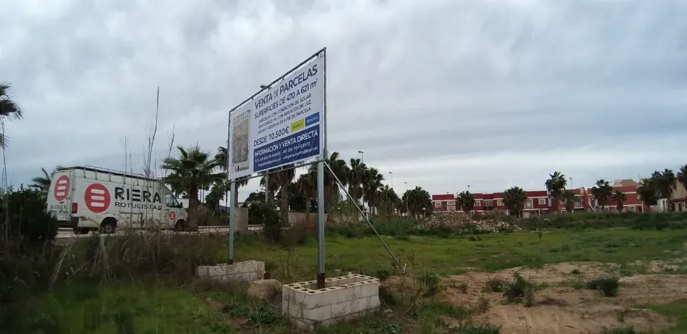 Cartel publicitario de un inmueble en un campo de hierba, furgoneta con el logotipo “RIERA” visible a la izquierda.