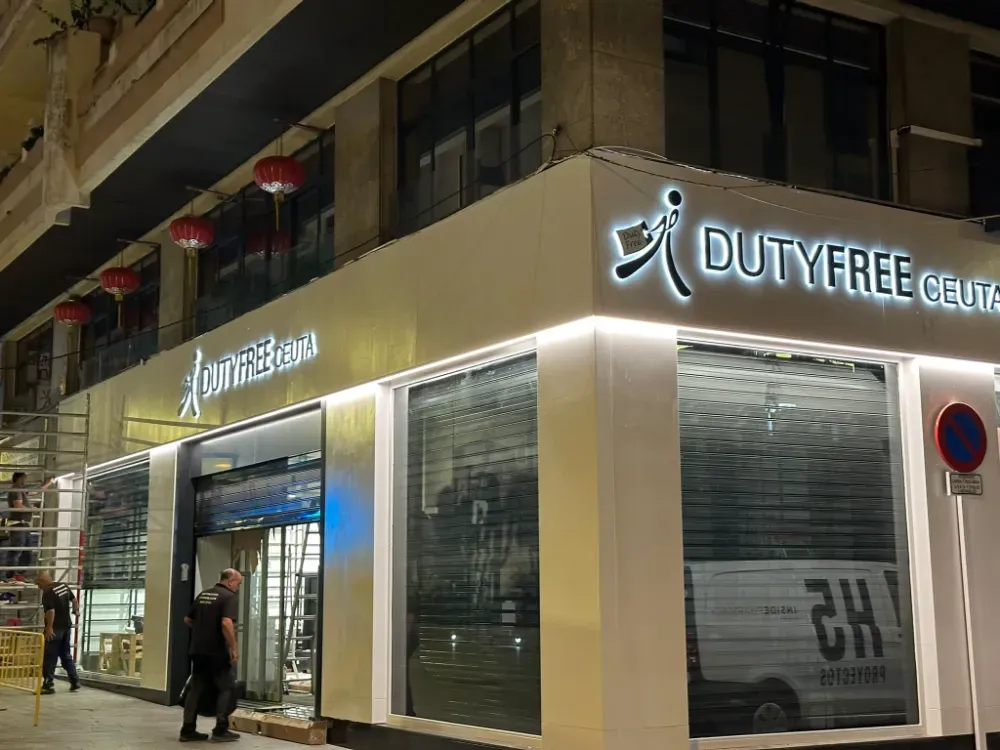 Exterior de tienda libre de impuestos por la noche con señalización iluminada y persianas de seguridad cerradas.