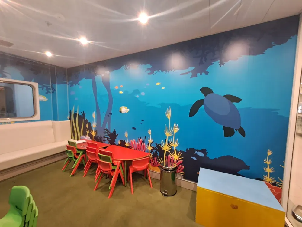 Zona de juegos infantiles con mural submarino, mesitas y sillas.