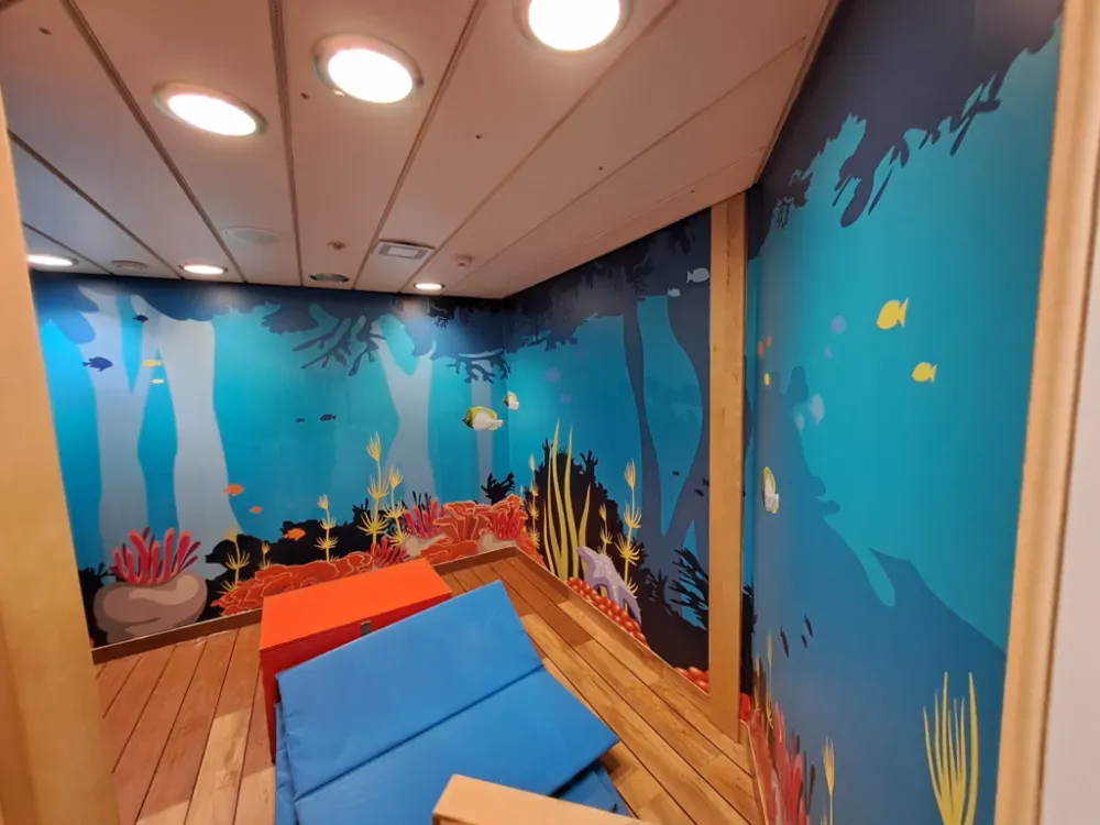 Sala de juegos con mural submarino, bloques de espuma y suelo de madera.