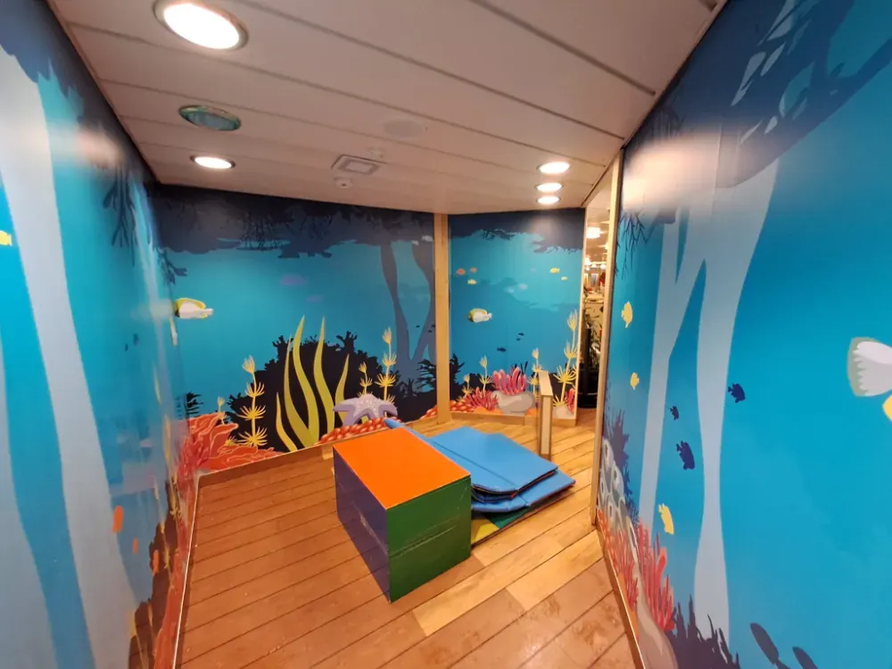 Pequeña área de juegos temática: paredes con temática oceánica de color turquesa, piso de madera y tapetes de juego.