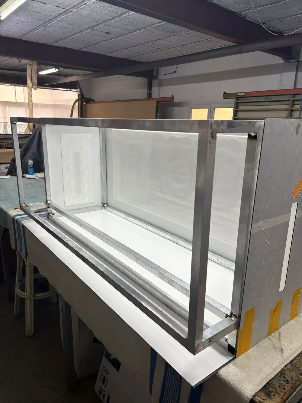 Caja con marco metálico y interior blanco, colocada sobre una mesa. Tiene un lateral abierto.