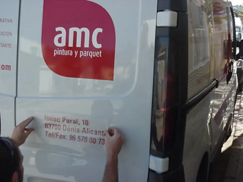 Manos colocando una pegatina en una furgoneta blanca con el logo de 