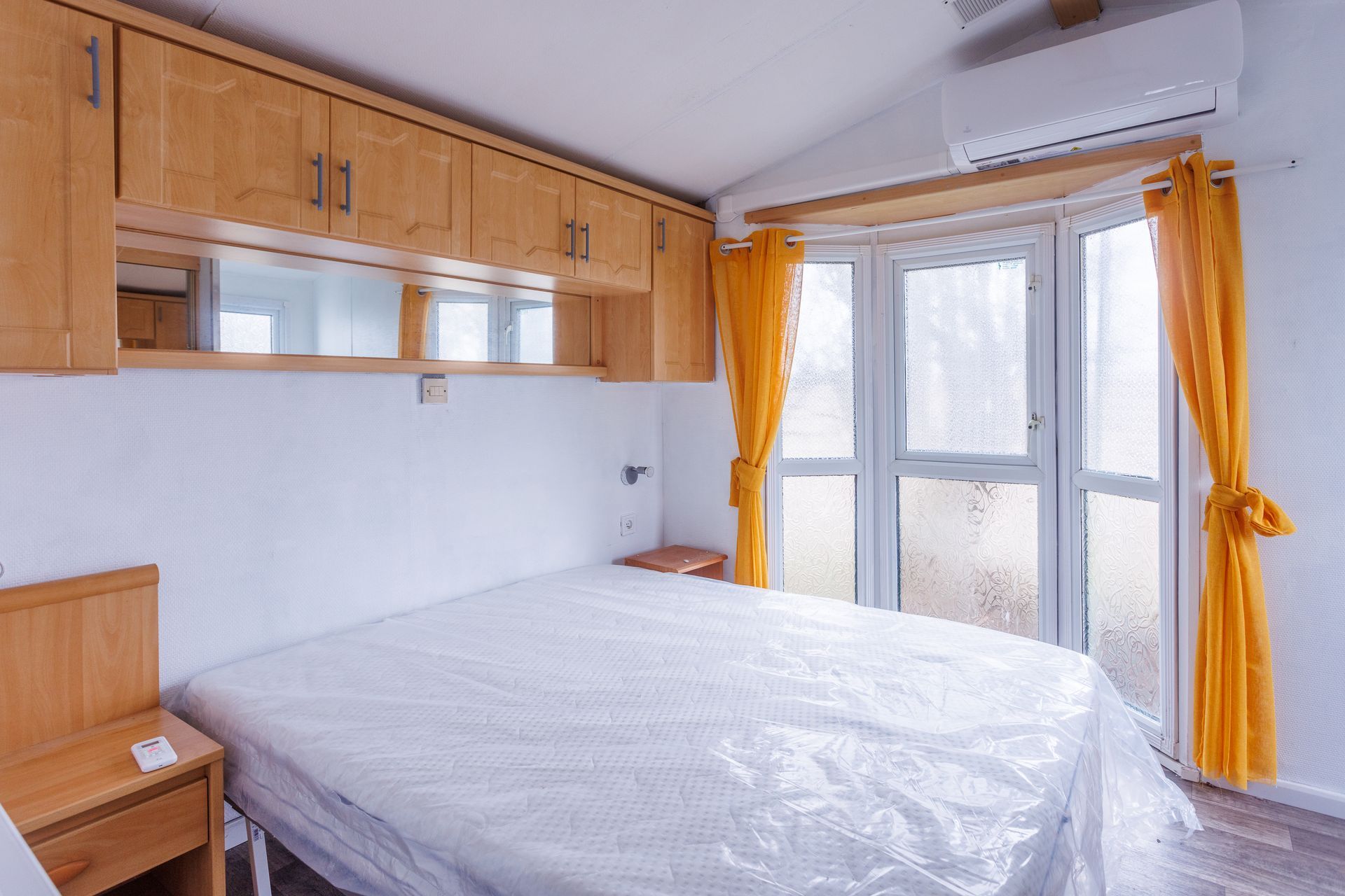 Chambre avec un lit, des armoires et une porte donnant sur l'extérieur ; rideaux orange.