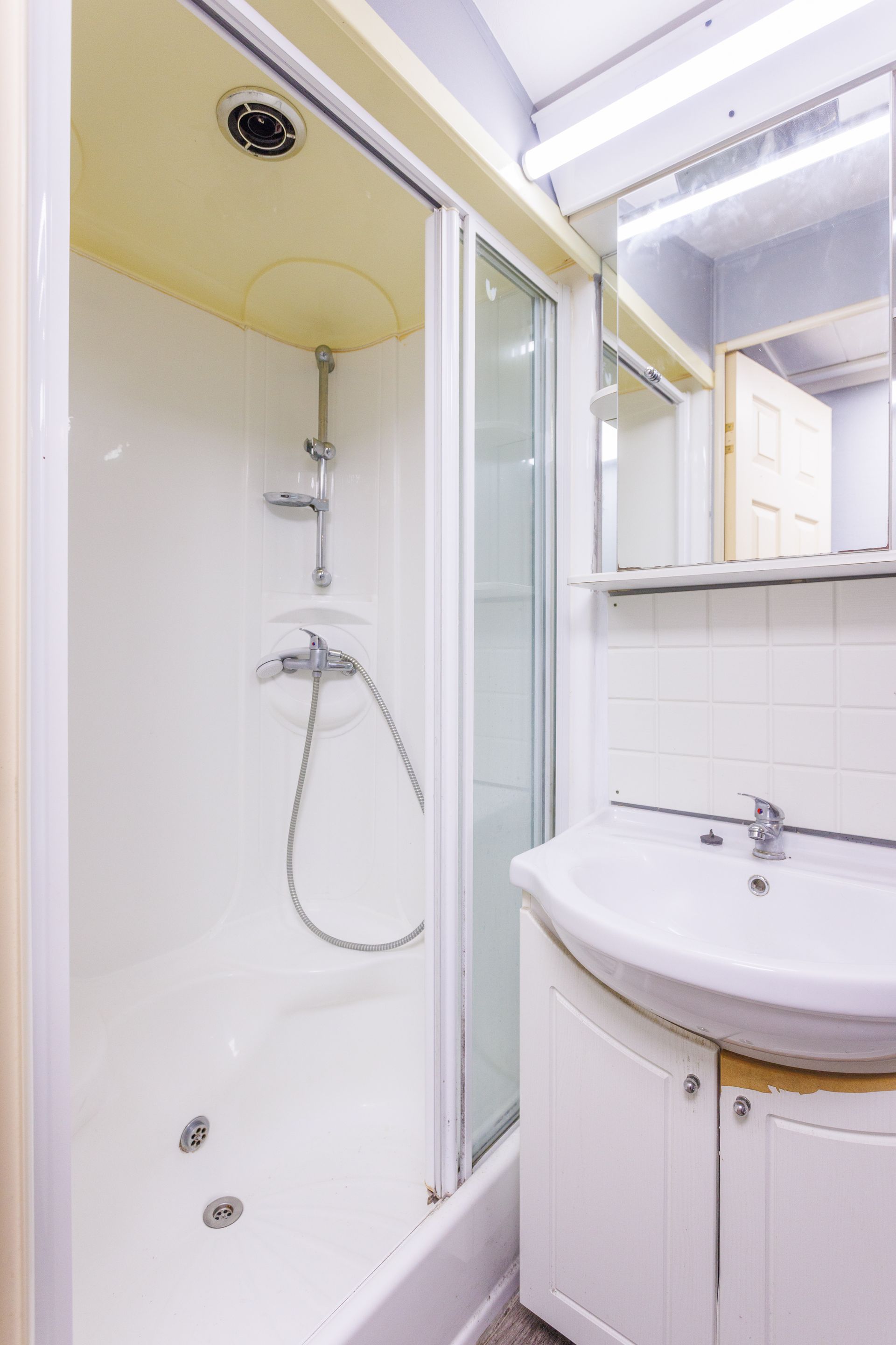 Petite salle de bain blanche avec douche, lavabo et miroir.