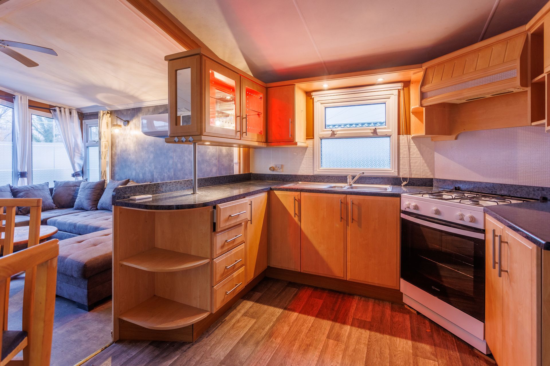 Une cuisine avec des placards en bois, une cuisinière et un plan de travail, attenante à un salon avec un canapé.