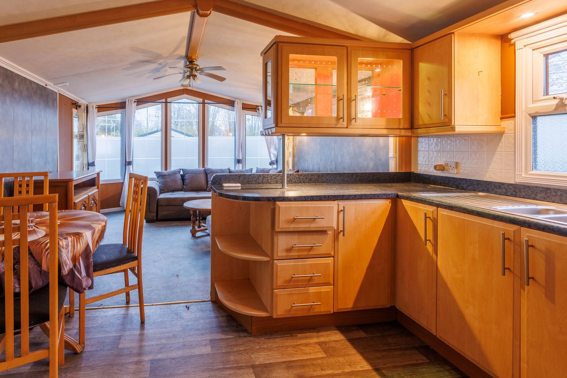 Intérieur d'une cuisine et d'un séjour avec placards, plans de travail et meubles en bois.