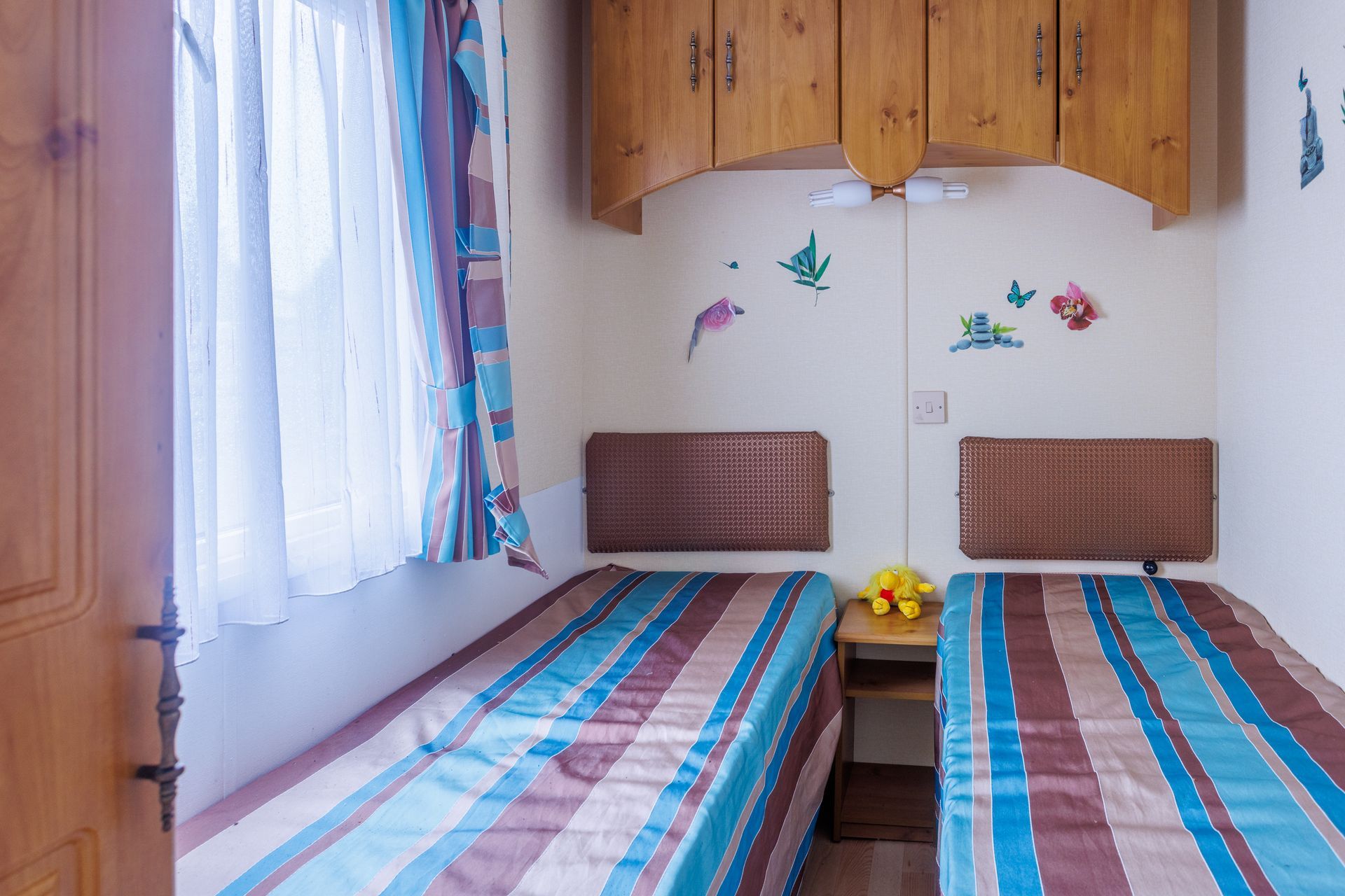 Petite chambre avec deux lits jumeaux, linge de lit à rayures colorées et une petite table de chevet.