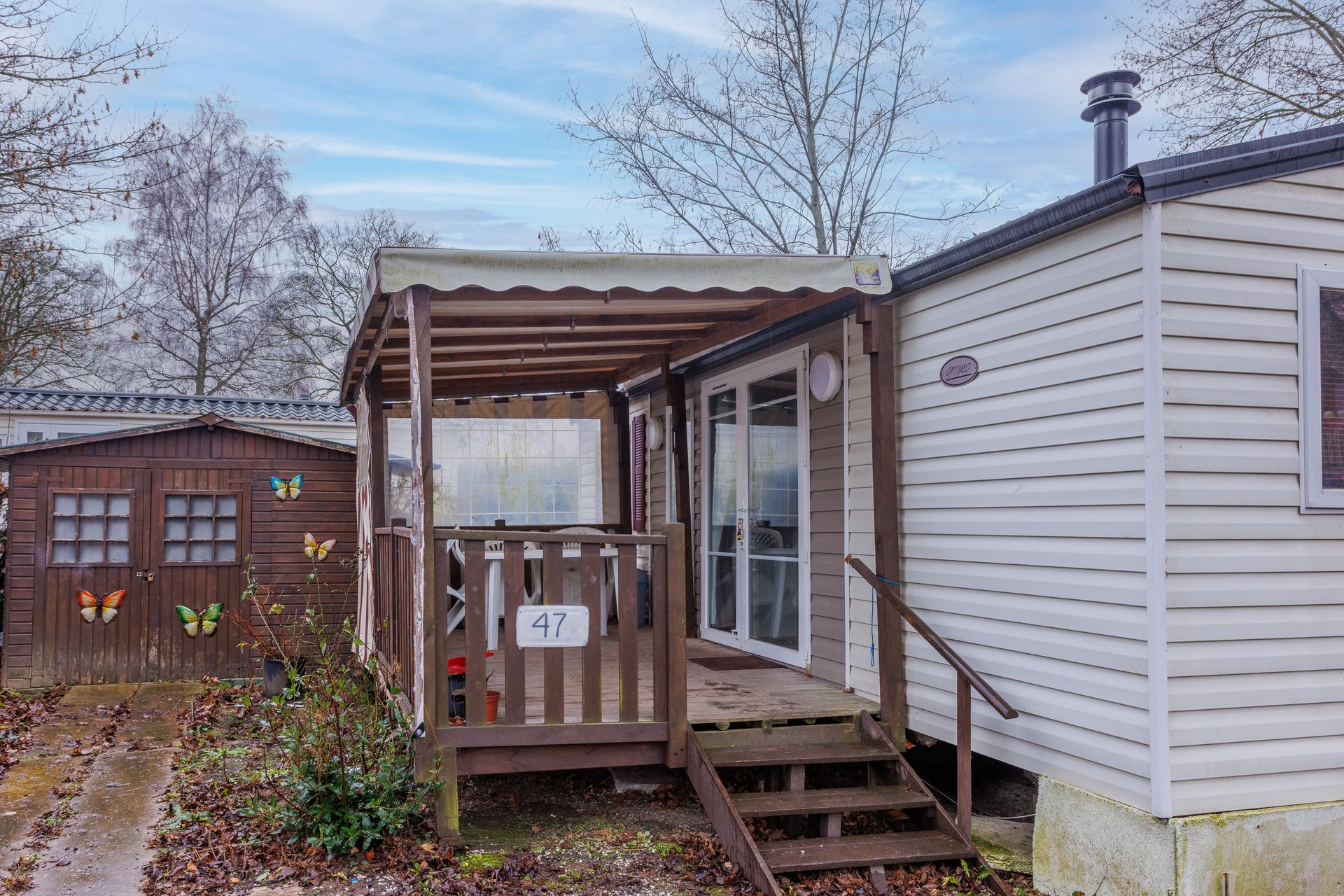 Terrasse extérieure avec table à manger, chaises, chaise longue et barbecue ; un bâtiment en bois avec de grandes fenêtres est visible en arrière-plan.