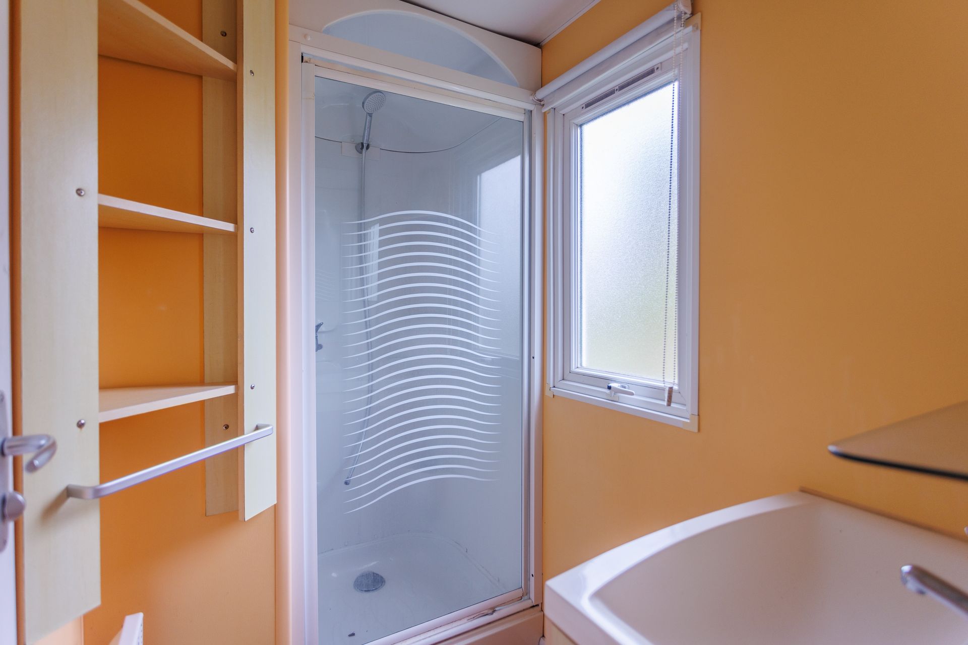 Salle de bains avec douche, étagères, baignoire et fenêtre ; murs orange.