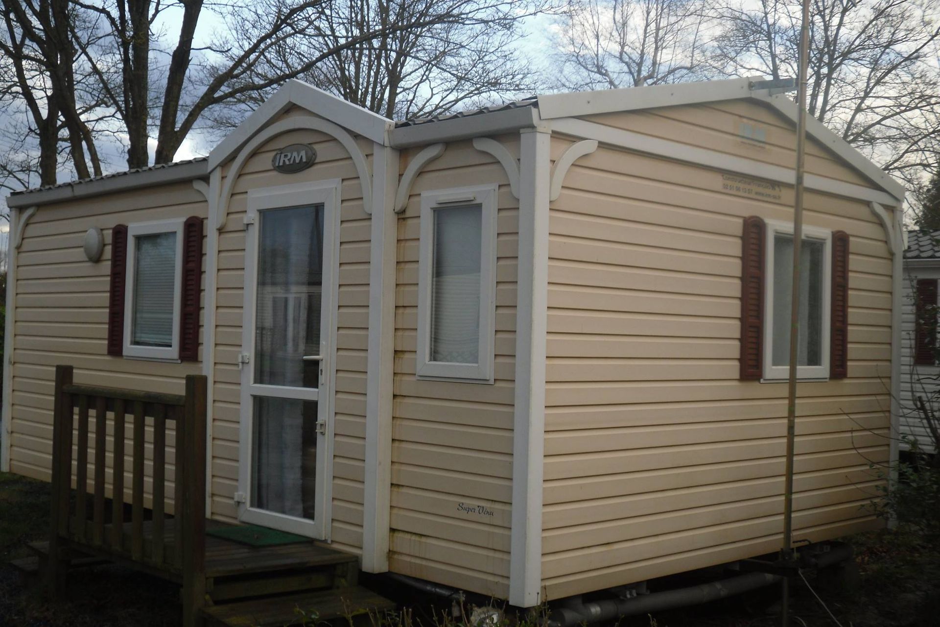 Mobil-home beige clair avec finitions blanches et volets bordeaux.