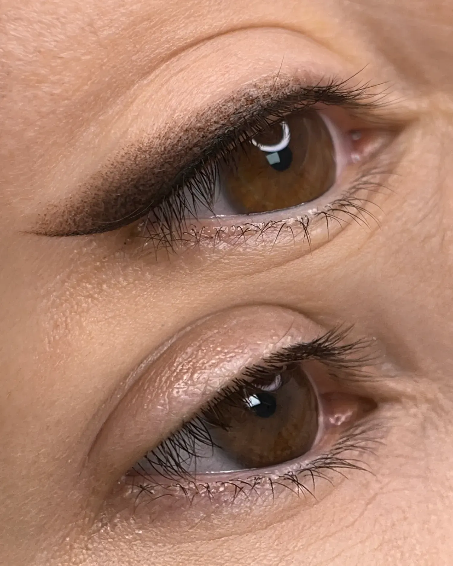 Primer plano de dos ojos marrones, el superior con delineador y el inferior sin, mostrando el efecto antes y después.