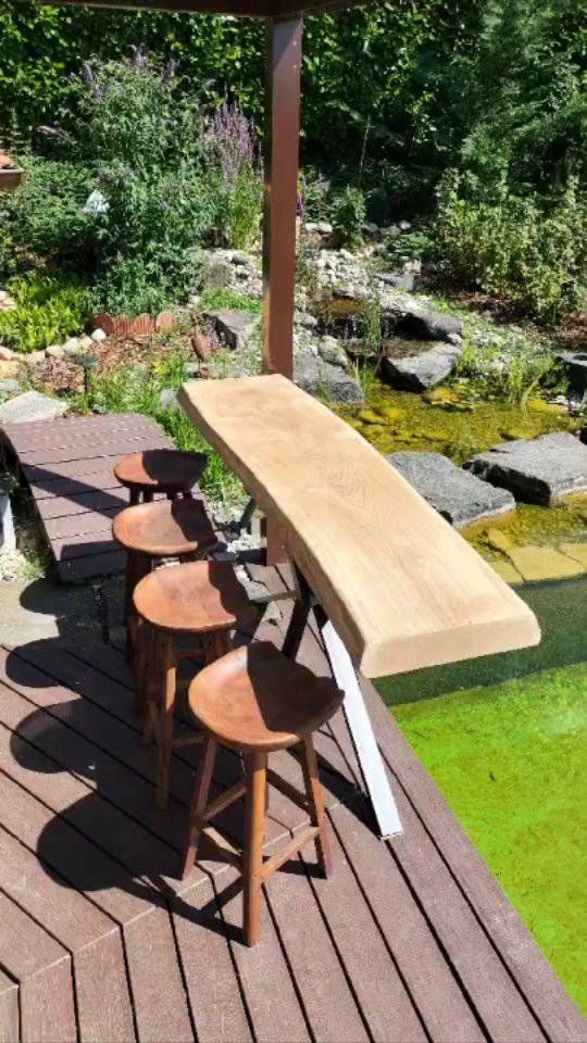 Une terrasse en bois avec une table et des tabourets à côté d'un étang. Photo D'équerre et d'aplomb