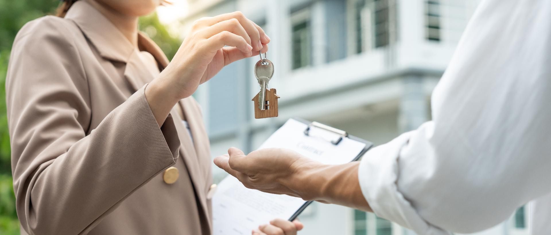 Ein Immobilienmakler übergibt einer Person vor einem Haus die Schlüssel.