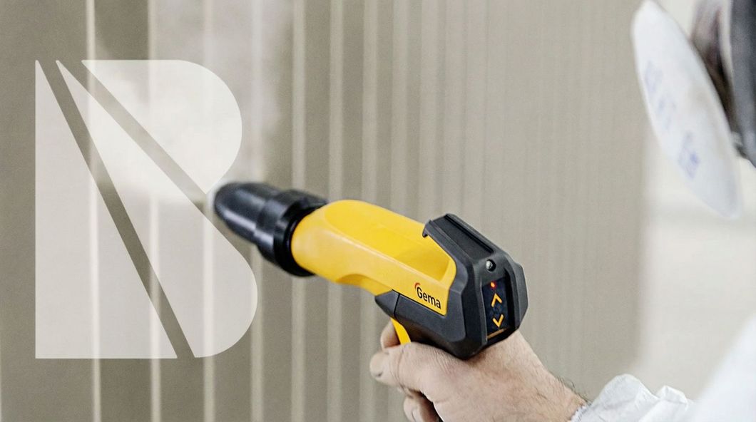 Eine Person, die eine Wand mit einer gelben Pulverbeschichtungspistole besprüht, trägt dabei eine Atemschutzmaske.