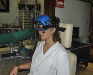 Mujer con auriculares médicos azules, sentada en una silla blanca. Se encuentra en un centro médico, posiblemente una clínica oftalmológica.