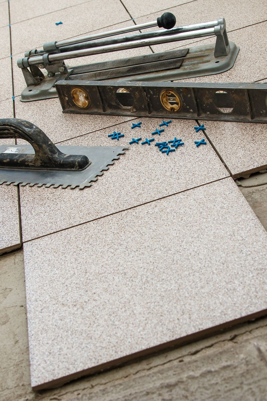 Pose de carrelage en cours. Sur les carreaux, sont posés le niveau, la carrelette, la truelle et les croisillons.