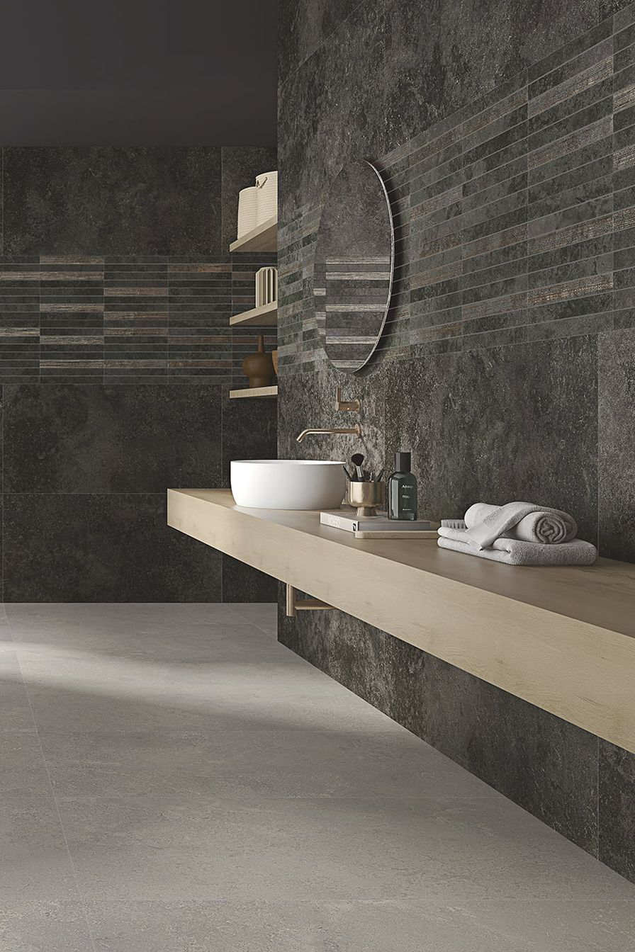 Salle de bains moderne avec mur texturé foncé, meuble-lavabo et étagères en bois clair, miroir rond et sol gris.