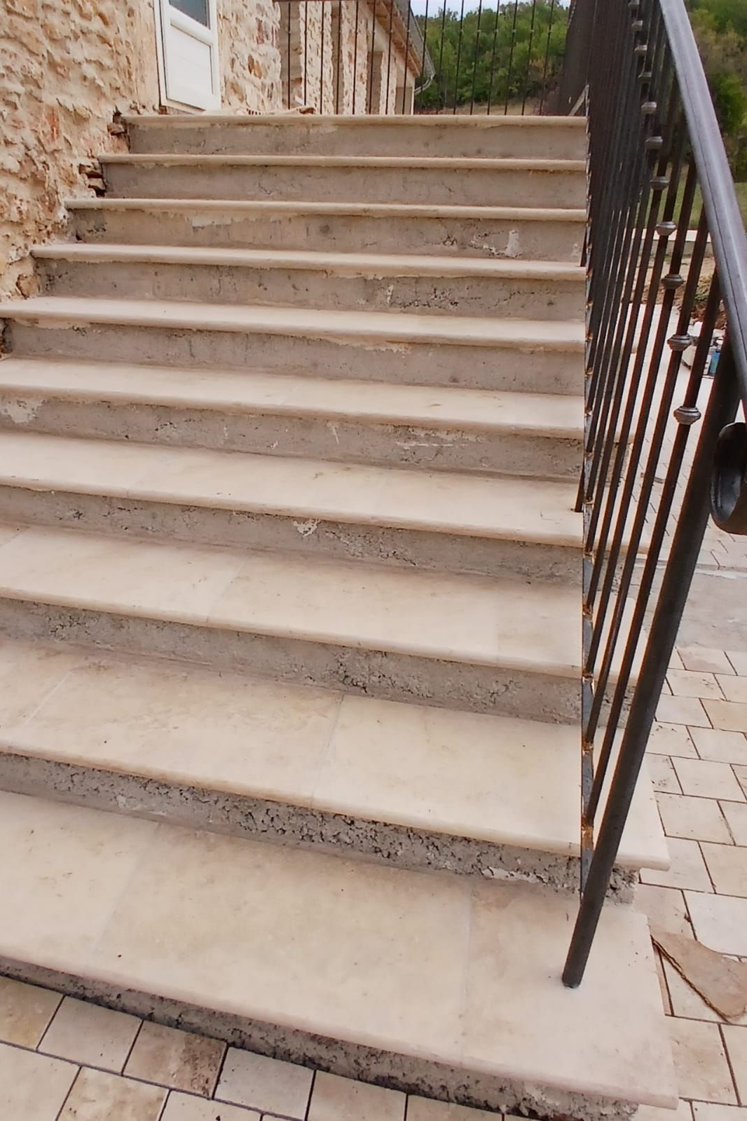 Des marches en pierre mènent à un bâtiment, avec une rambarde en métal noir sur la droite.