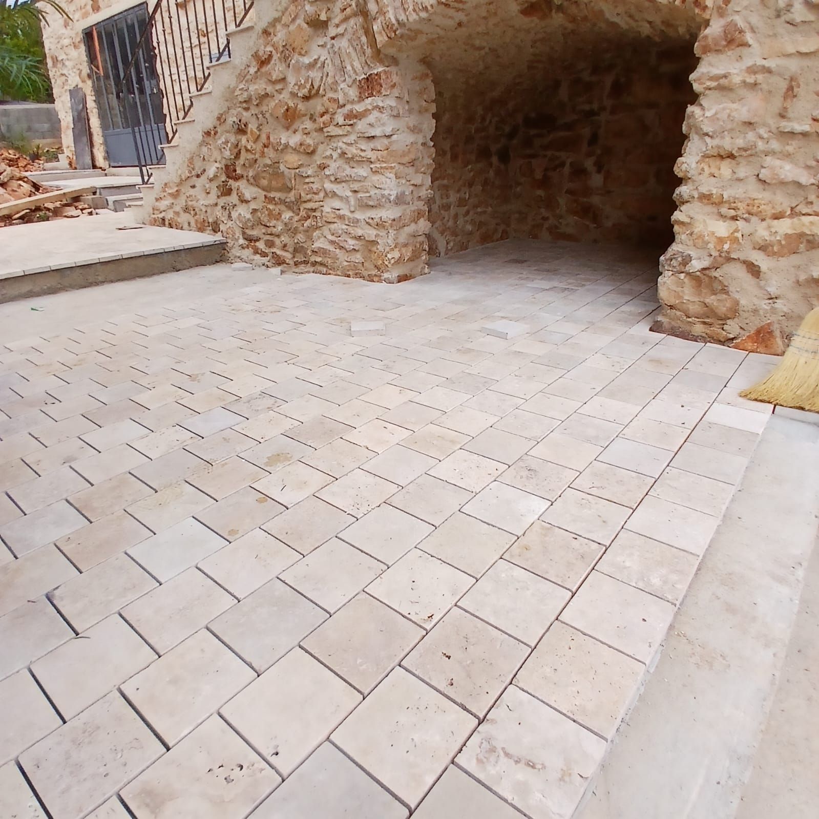 Terrasse en pierre à surface texturée, menant à une entrée voûtée en pierre.