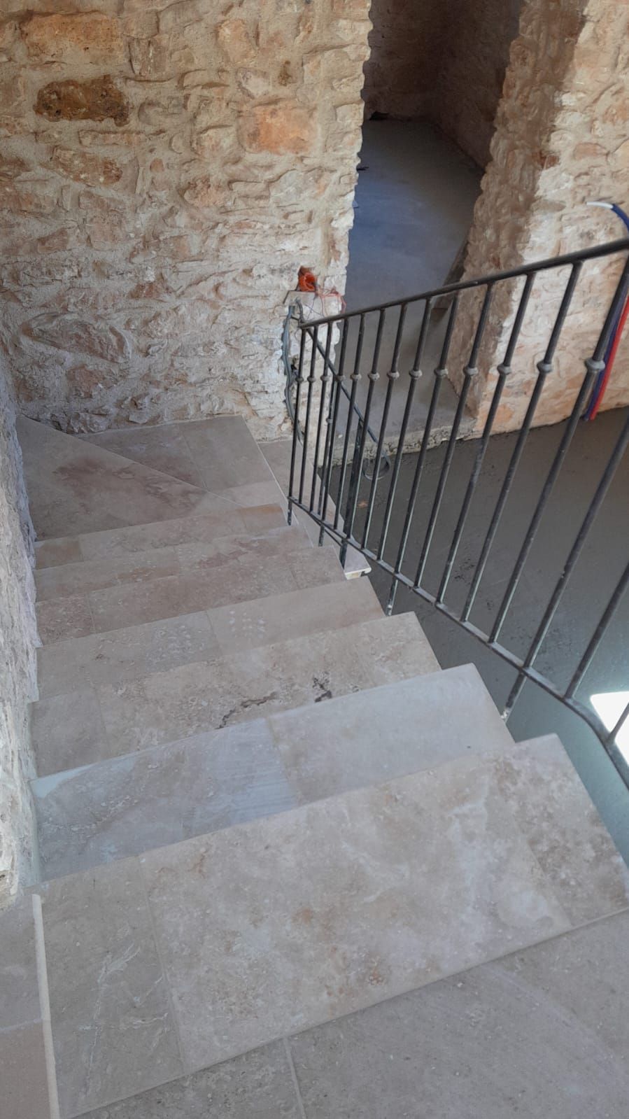 Escalier en pierre avec rampe en fer noir, descendant d'une porte en pierre.