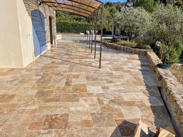 Terrasse en pierre avec pergola, donnant sur un jardin. Dalles de pierre beige et marron.
