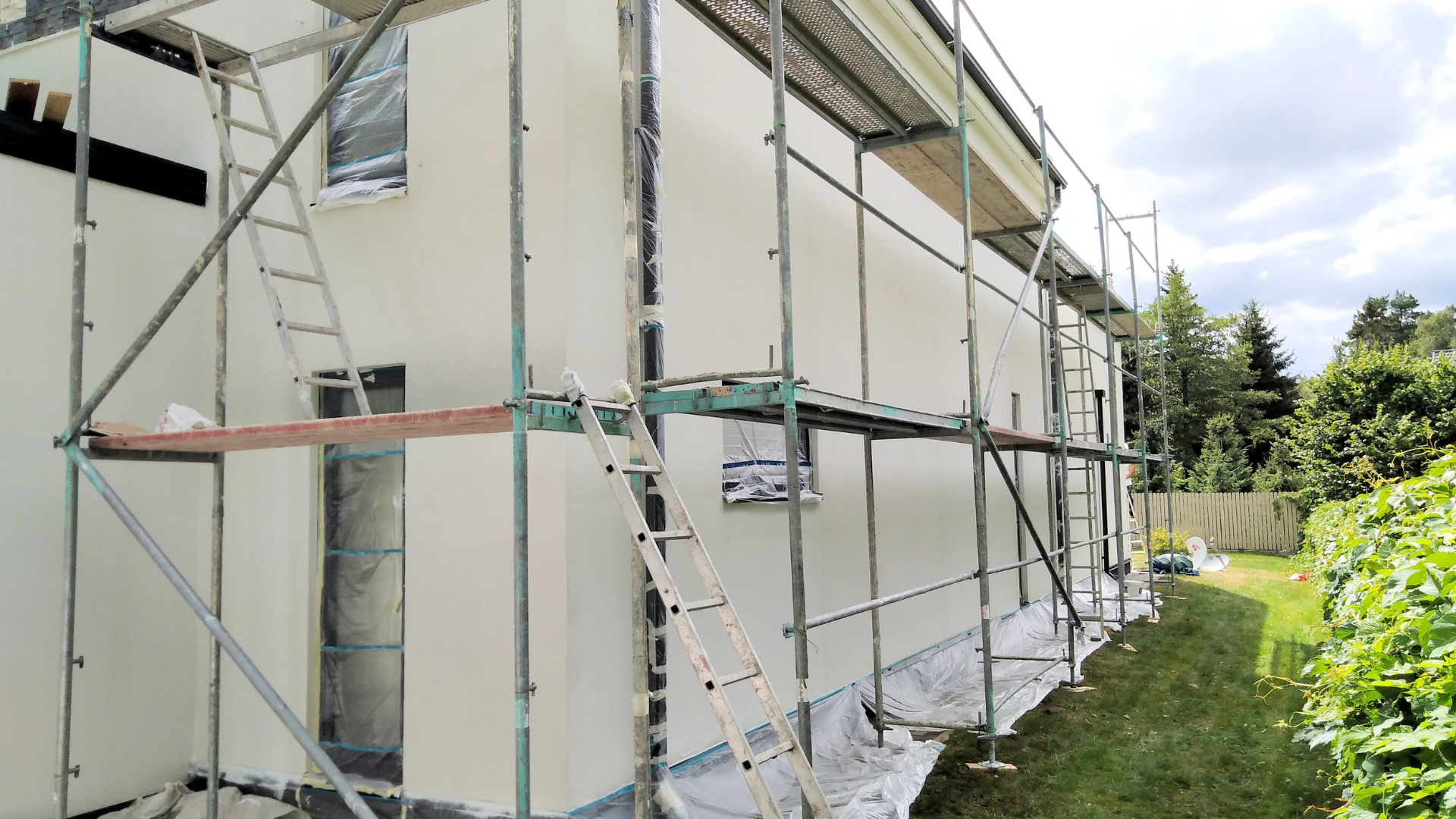 Façade de la maison en rénovation, avec échafaudages et échelle, peinte en blanc.
