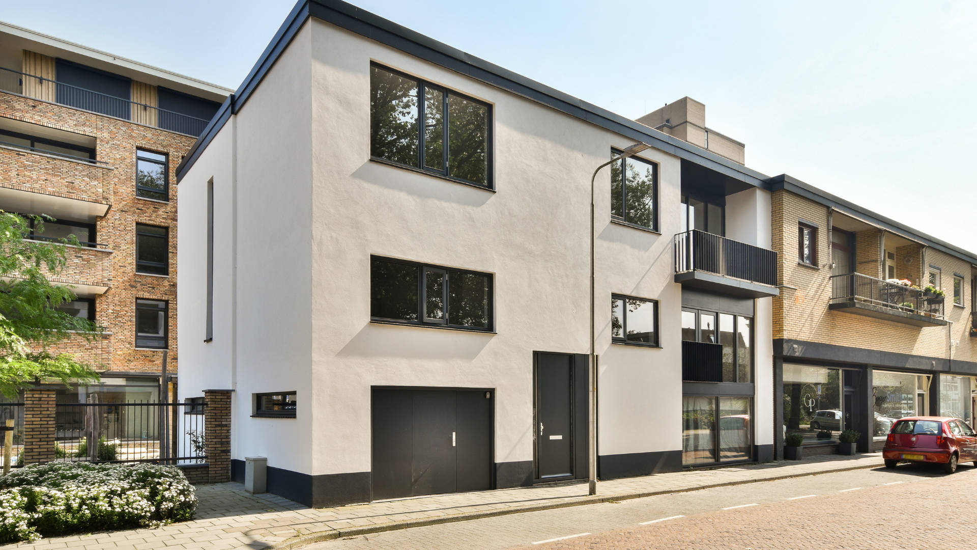 Bâtiment blanc de deux étages avec des boiseries, des fenêtres et une porte de garage noires, situé dans une rue.