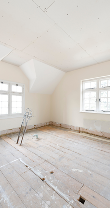 Pièce en rénovation, parquet apparent, échelle, deux fenêtres, plafond mansardé.