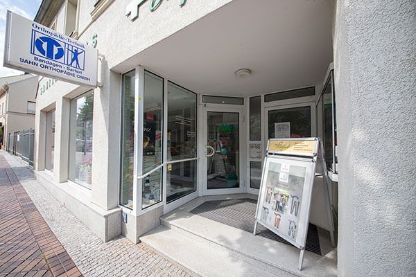 Eingang zu einem Gebäude mit einem Schild für eine Arztpraxis; Glastür, Bürgersteig und eine Sandwichtafel.