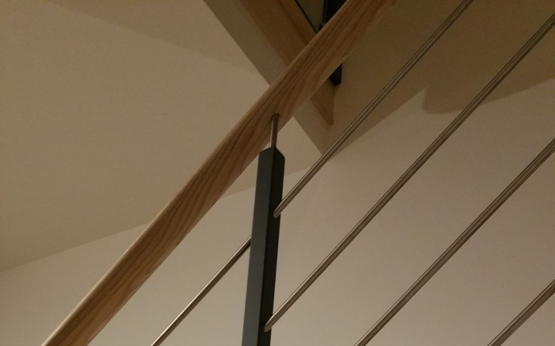Escalier avec marches et garde-corps en bois, support en métal noir et barreaux métalliques horizontaux.