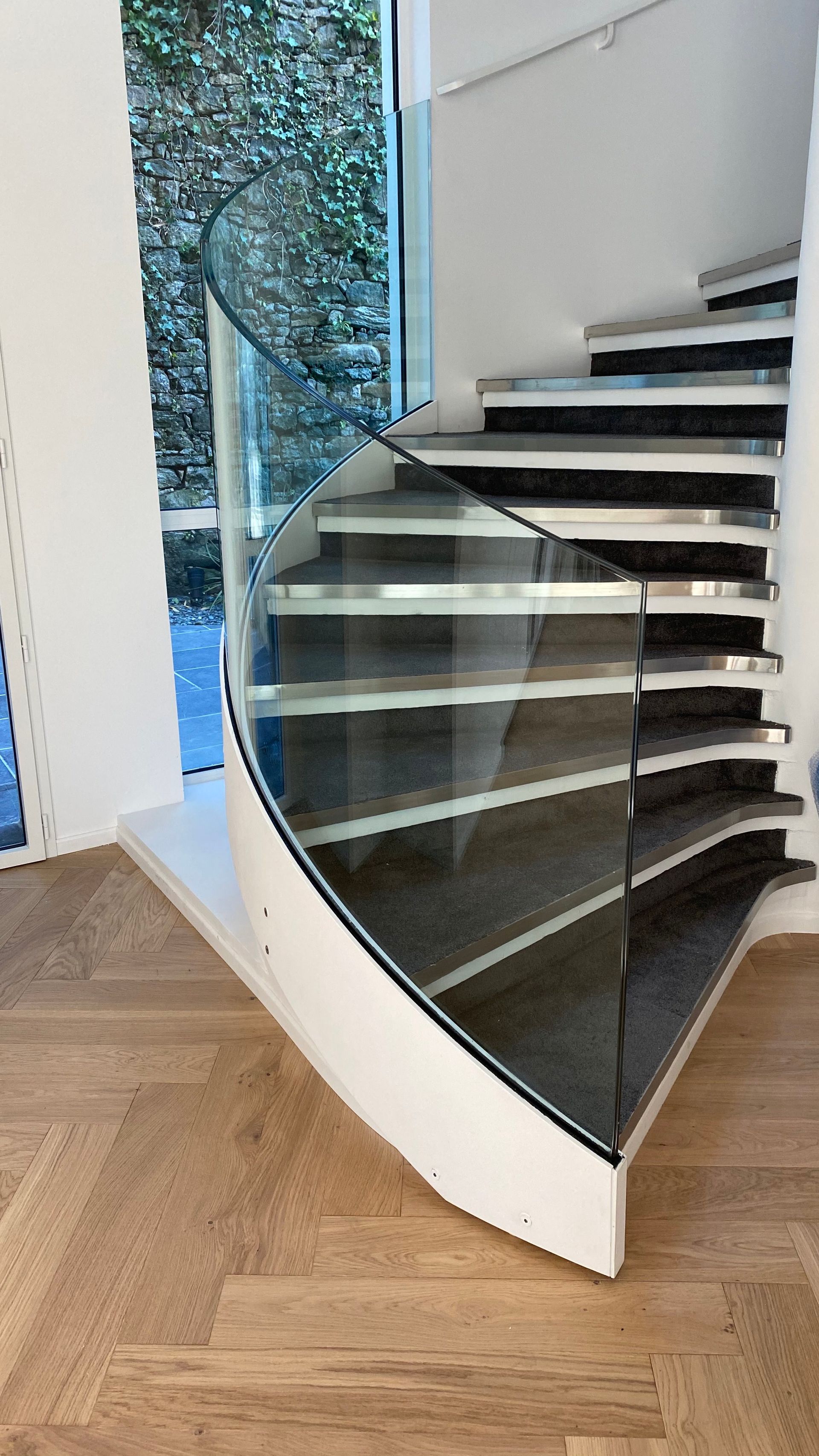 Escalier en colimaçon moderne avec garde-corps en verre, cadre blanc et marches en bois.