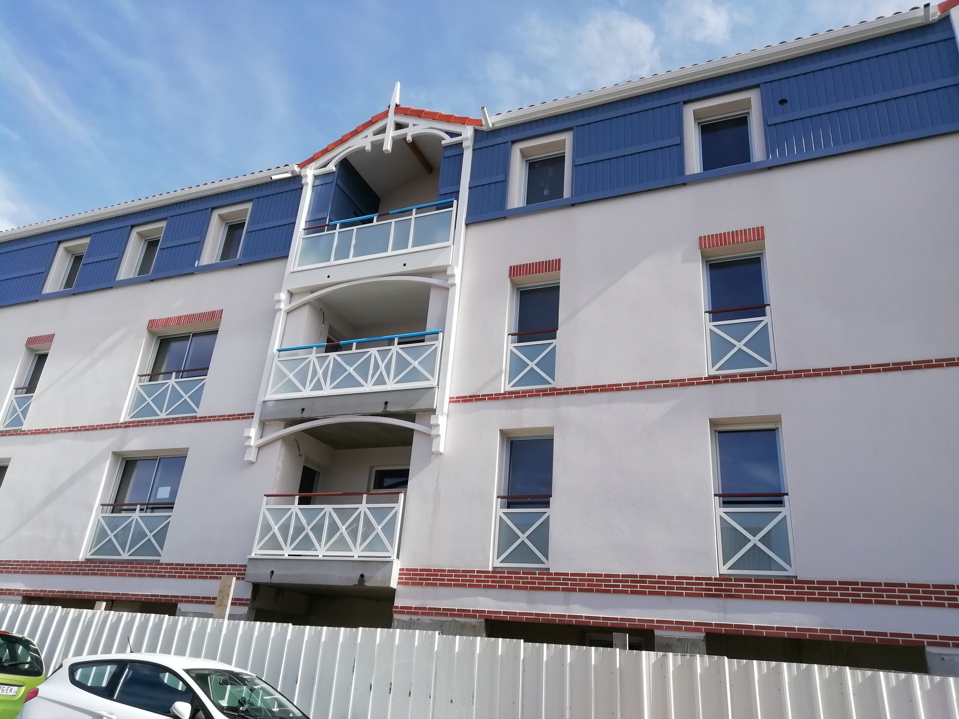 Immeuble d'appartements blanc et bleu avec balcons, sur fond de ciel bleu.