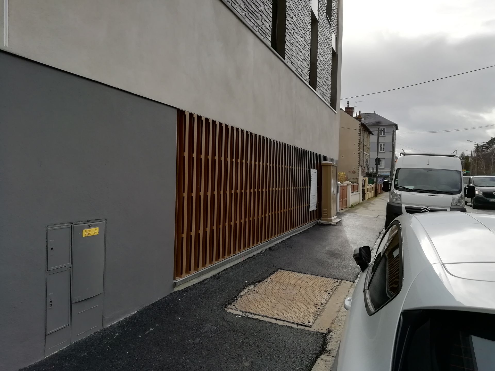 Extérieur d'un bâtiment avec brise-soleil. Une voiture et une camionnette sont garées dans la rue.