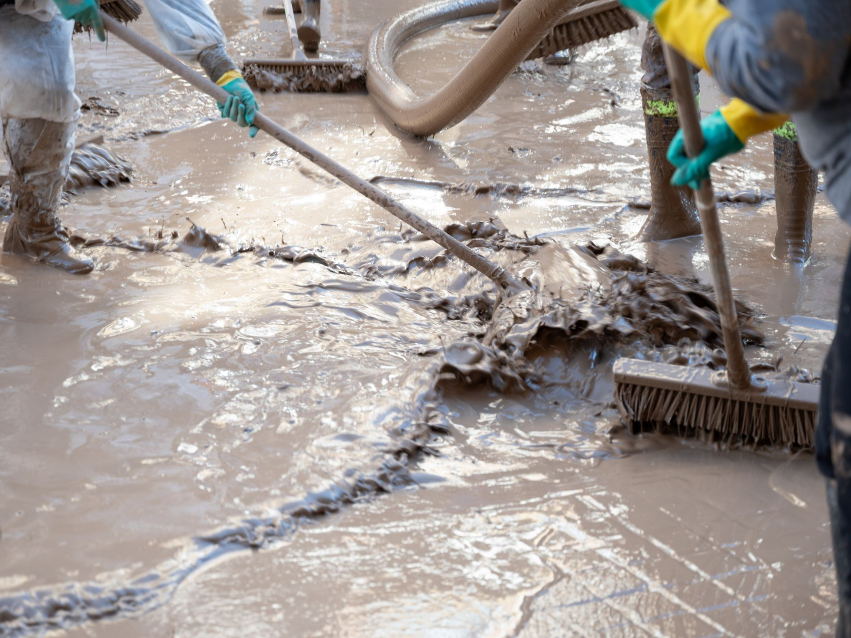 Des professionnels en train de nettoyer un sol boueux.