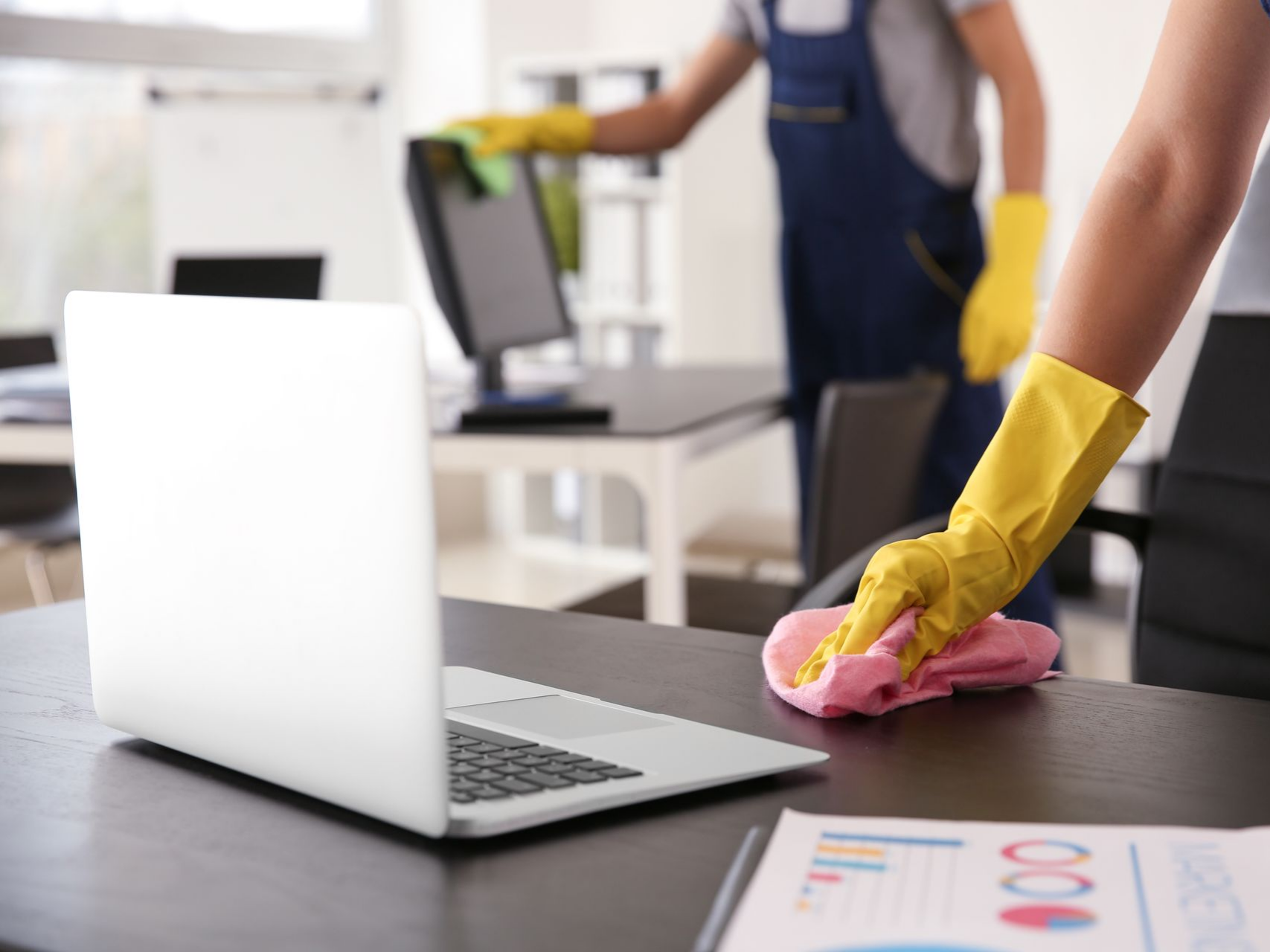 Une personne qui passe un chiffon sur un bureau où se trouve un ordinateur portable.