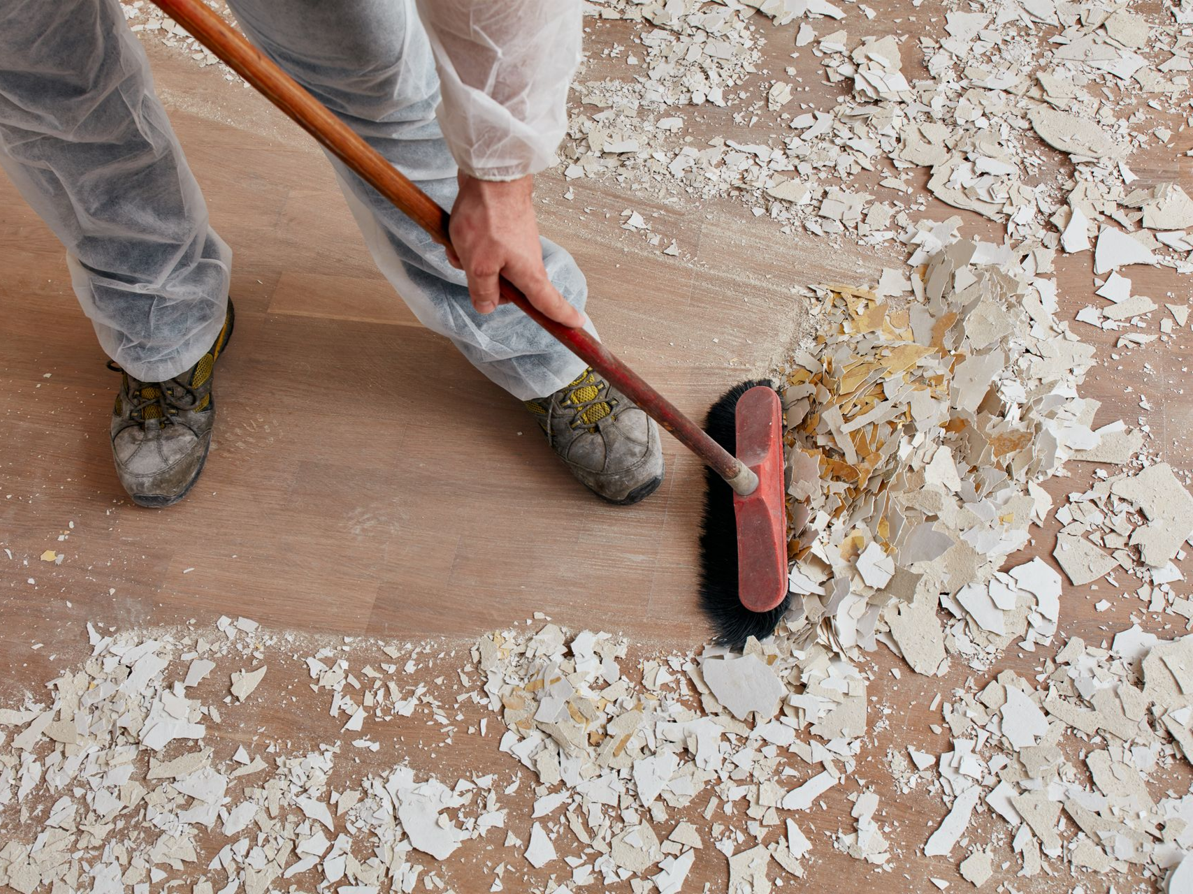 Une personne balaie des débris sur un plancher en bois à l'aide d'un balai-brosse.