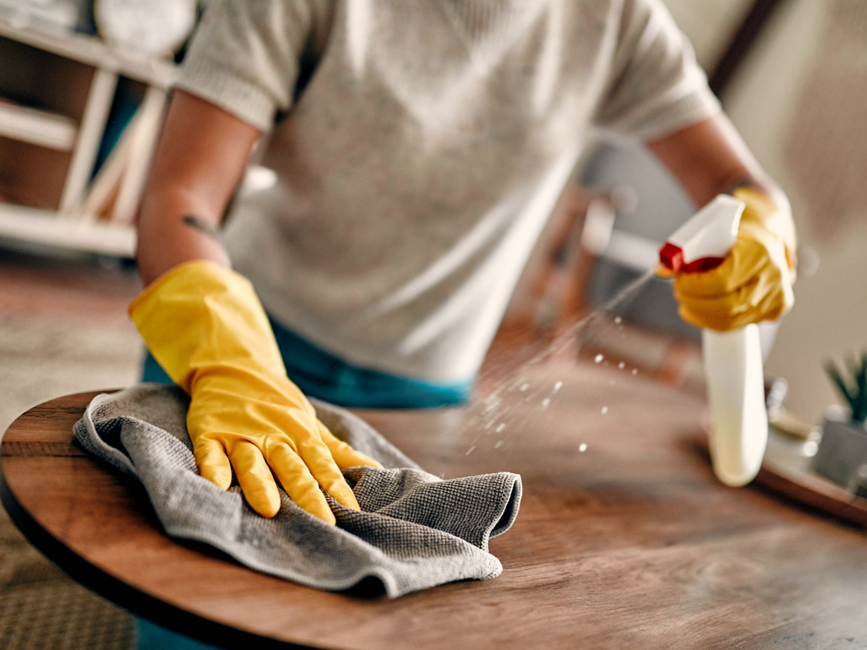 Une personne qui passe un coup de chiffon sur une table pour nettoyer les résidus de produits d'entretien.