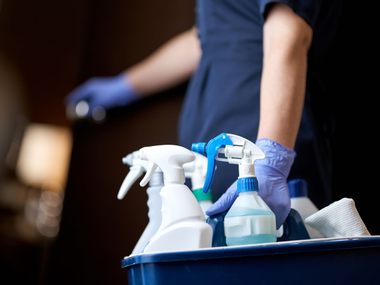 Une personne porte un bac avec des produits d'entretien.