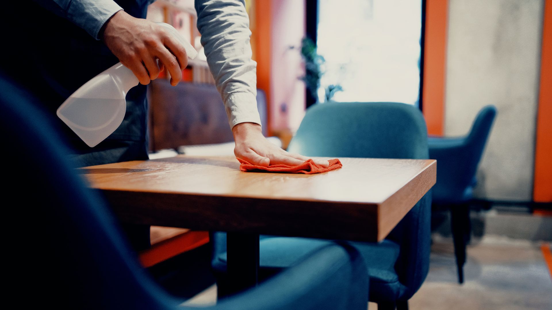 Un personne qui nettoie une table à l'aide d'un spray et d'un chiffon.