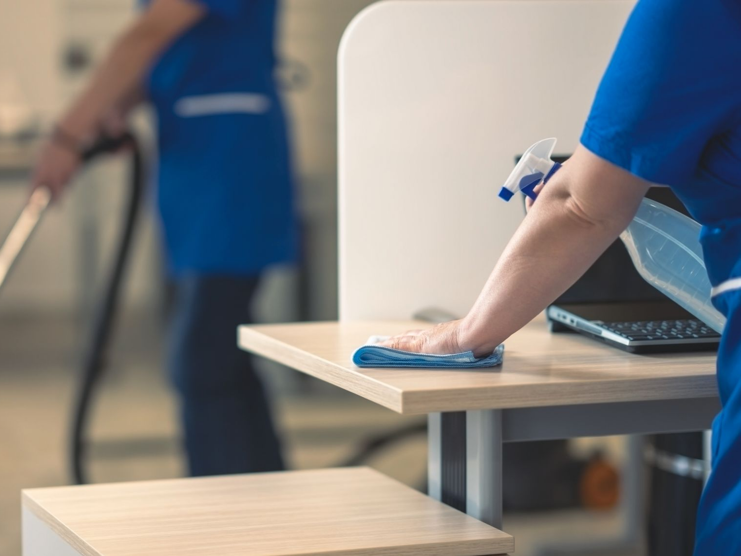 Une personne qui dépoussière un bureau avec un spray et un chiffon.