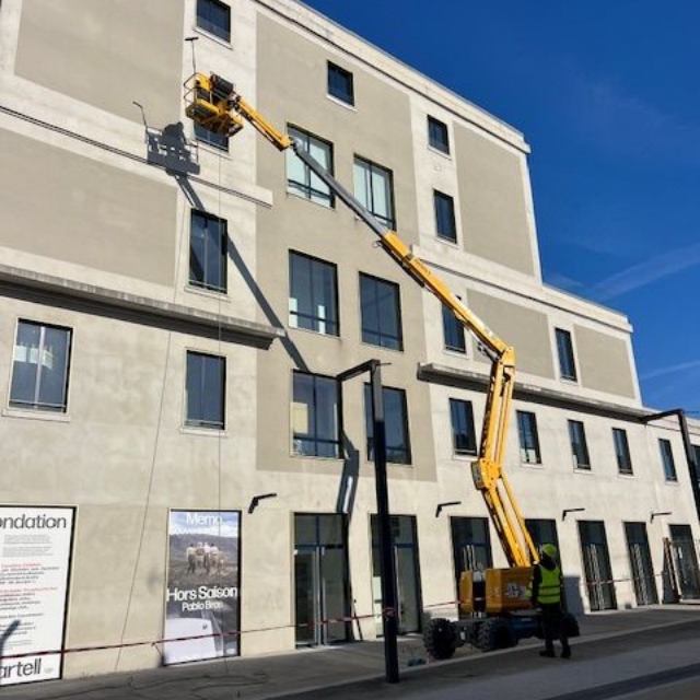 Un professionnel sur une nacelle qui nettoie une vitre en hauteur.