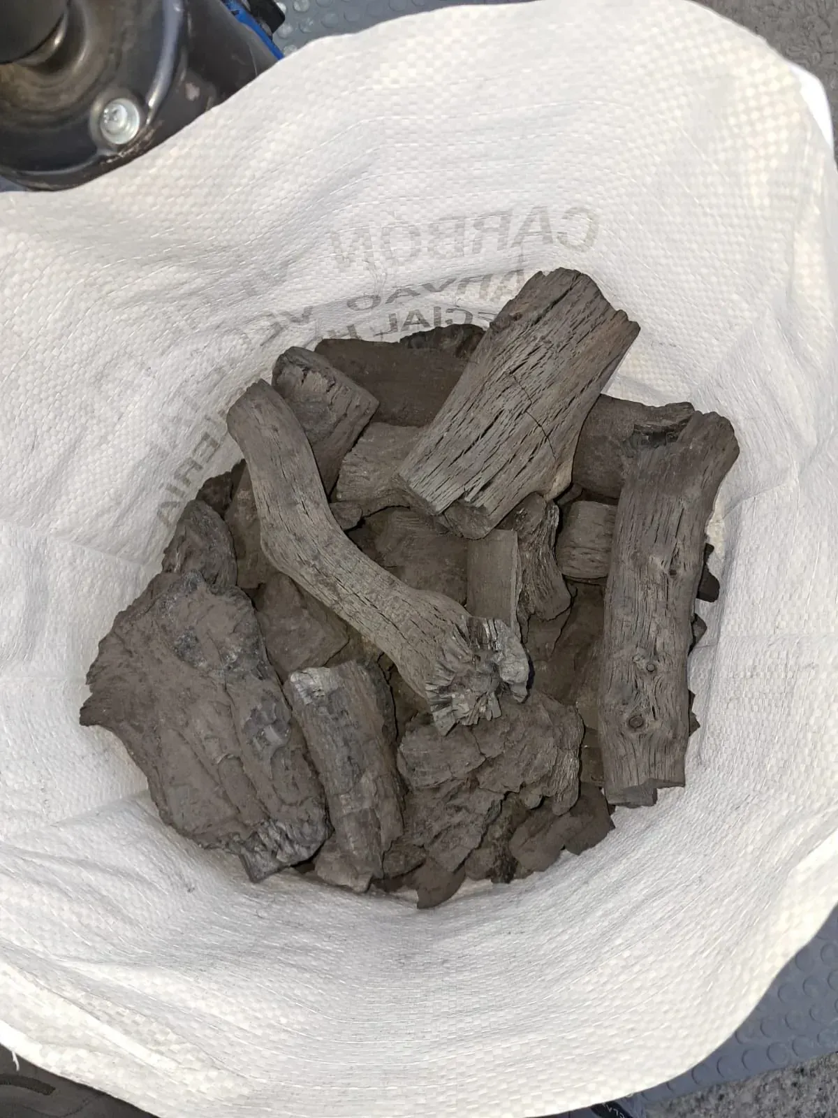 Bolsa de briquetas de carbón, de color gris oscuro, de forma cilíndrica e irregular, en una bolsa blanca.