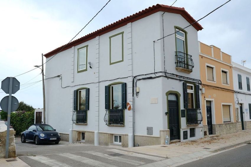 Casa de color melocotón bañada por el sol, con patio, pérgola y césped verde bajo un cielo azul.