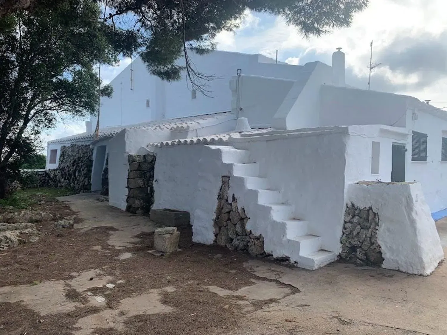 Casa de color melocotón bañada por el sol, con patio, pérgola y césped verde bajo un cielo azul.