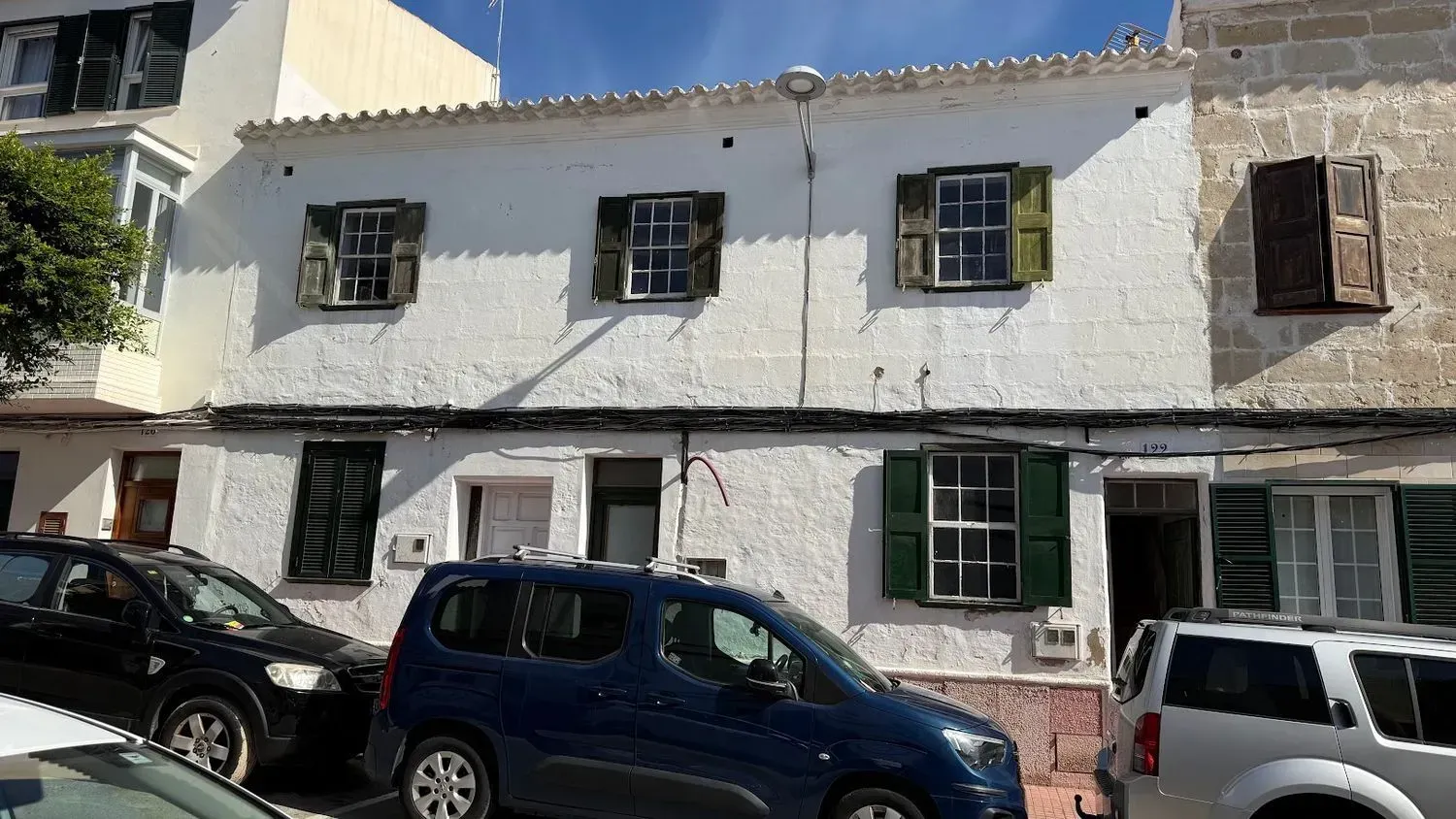 Cocina estrecha con armarios blancos, mesa y suelo de baldosas que da a una puerta luminosa.